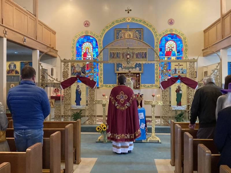 A priest faces the altar in a church, as parishioners pray. 
