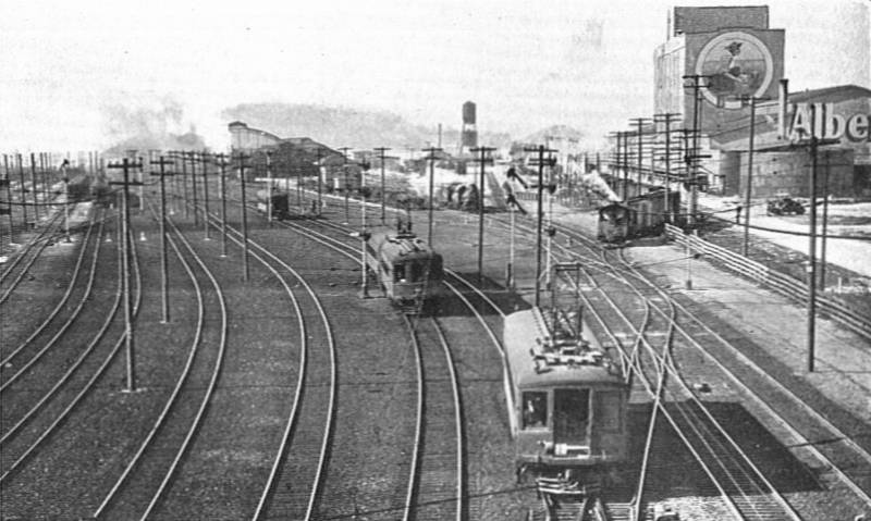 Black and white photo of multiple rail lines and trains exiting a busy train station.