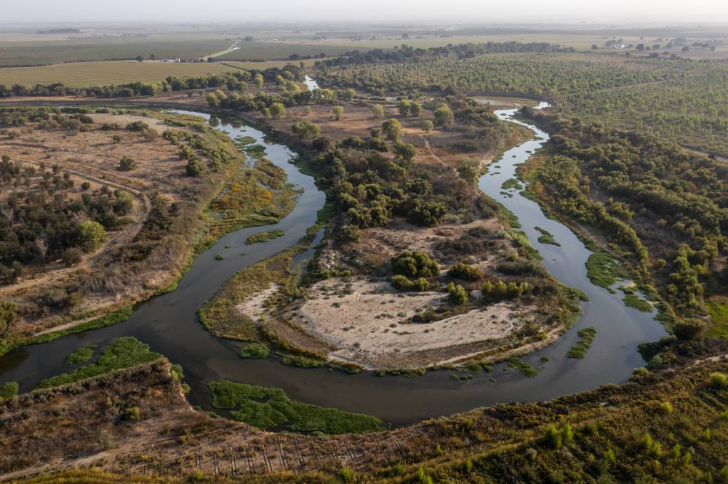An aerial view of two rivers snaking from the left and the right through a landscape of brown scrub and dark green trees. Where the rivers meet, they move off to the left of the photo.