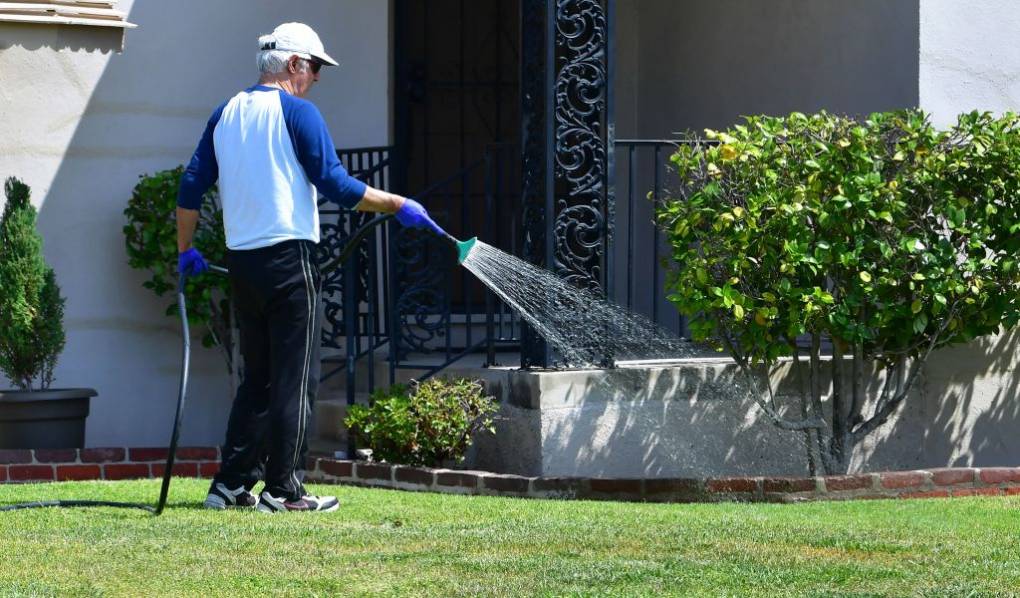 A man holds a hose to water a lawn outside.