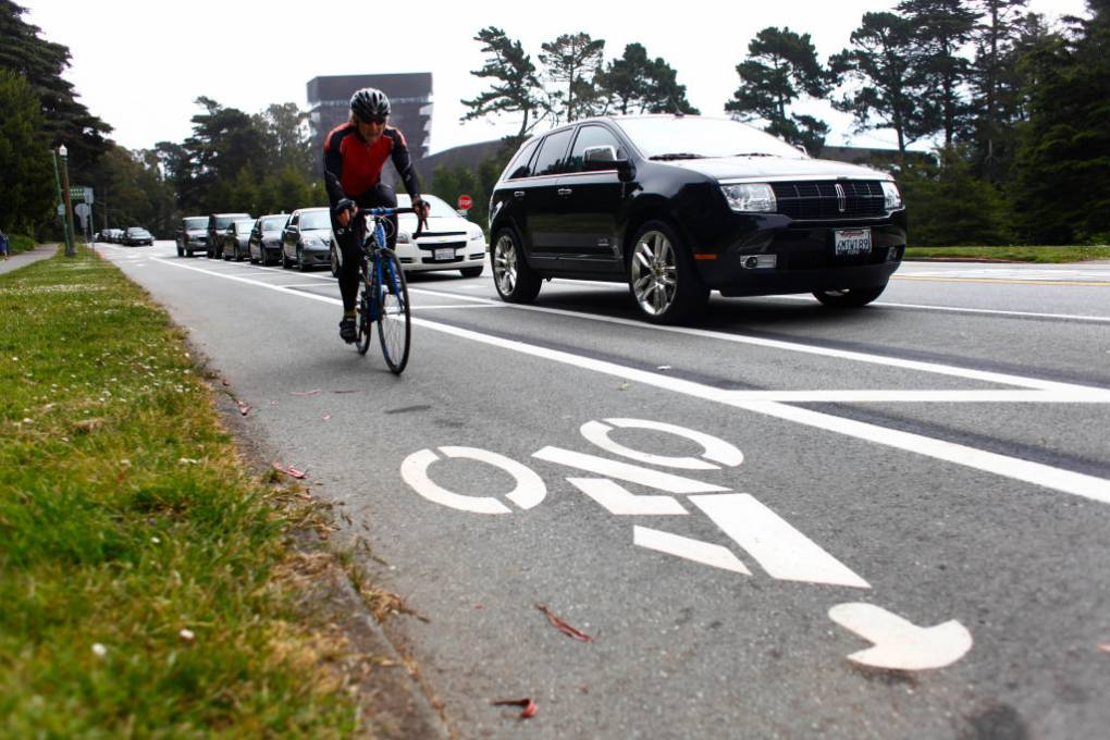 A man rides a bike in the bike lane and cars drive down the road.