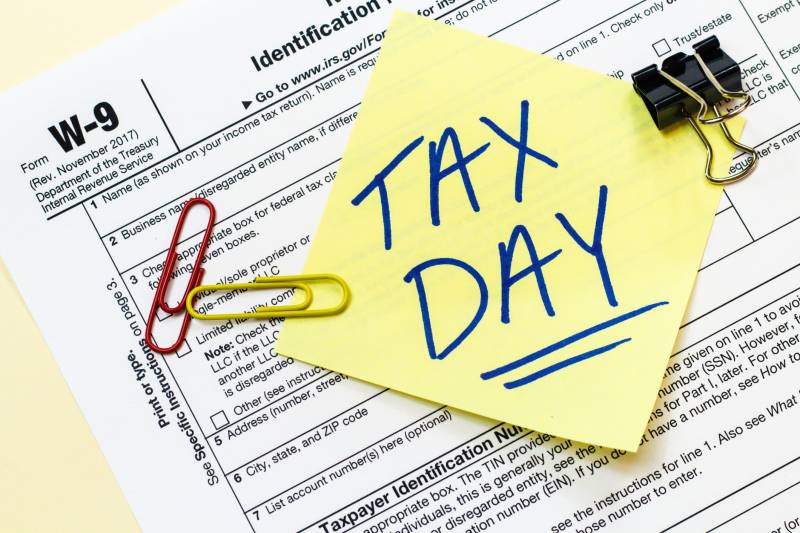 A sticky note that says "Tax Day" is posted on a W-9 form.