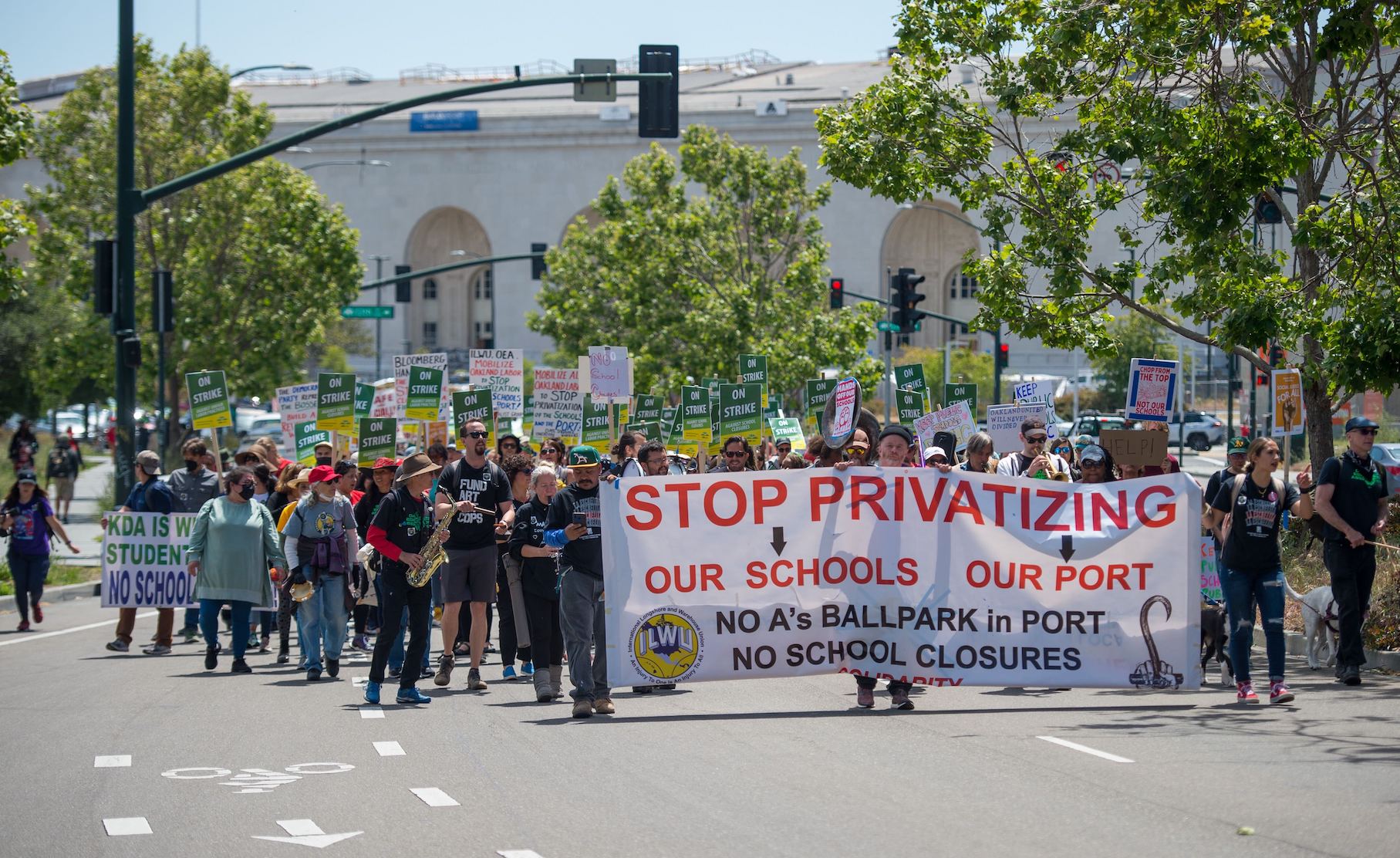 People march down a street, holding a banner that says 'Stop Privatizing Our Schools, Our Port"