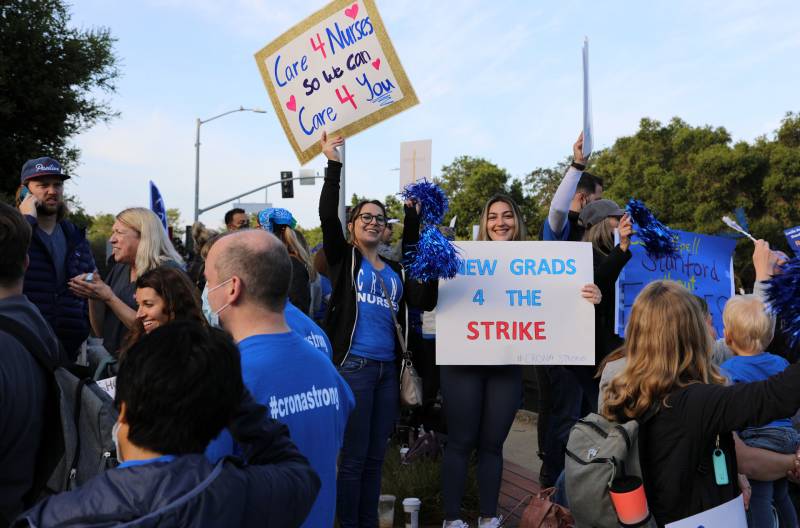 nurses wearing bright blue union shirts hold signs reading 'care 4 nurses so we can care 4 you'