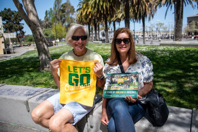 A man and Women hold Oakland A's Fan Gear on a sunny day
