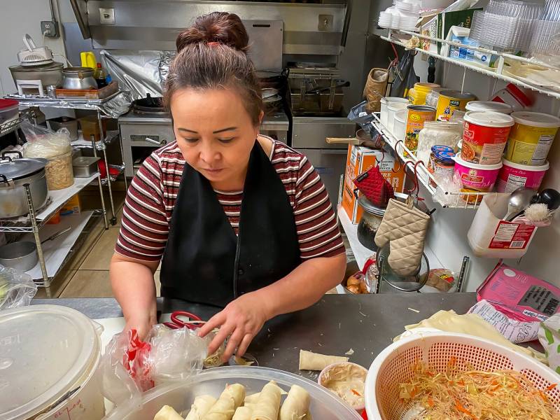 Woman with ponytail and apron works with dough in kitchen of restaurant