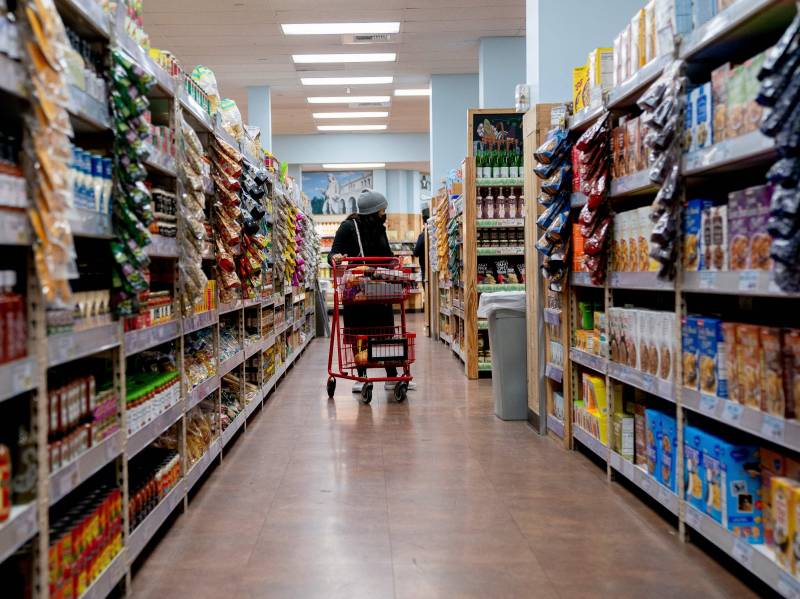 A person pushes a shopping cart in the aisle of a grocery store.