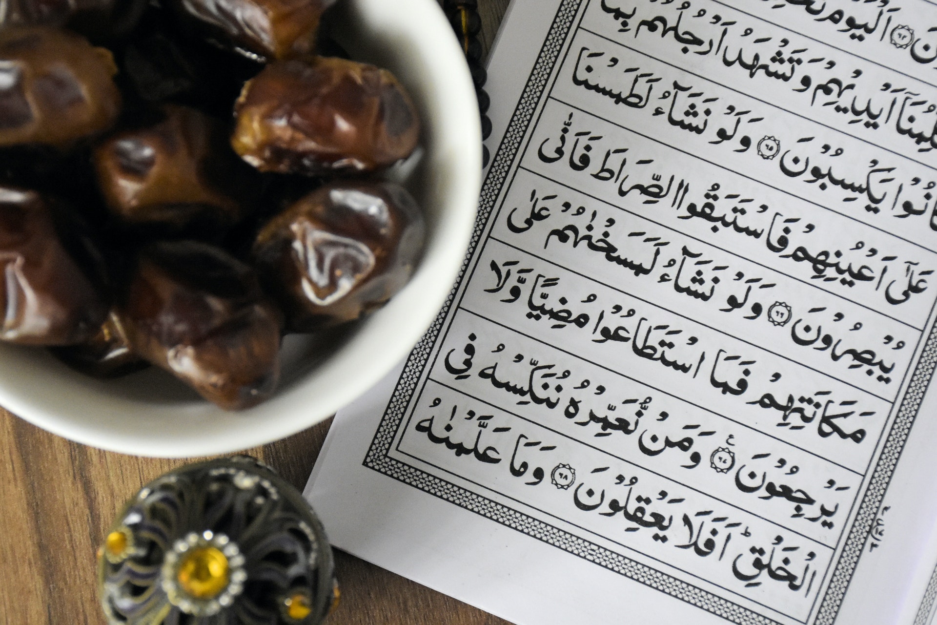 A bowl of dates on a table, next to a page of the Quran