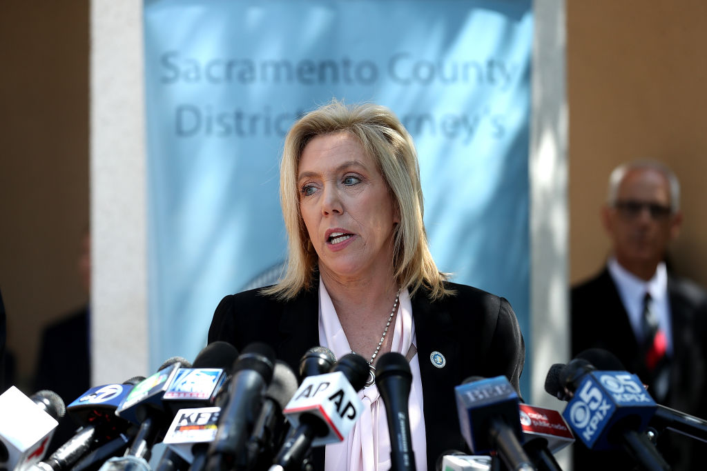 A woman speaks into a gaggle of media outlet microphones. Behind her is a sign that says, 'Sacramento County District Attorney's Office.'