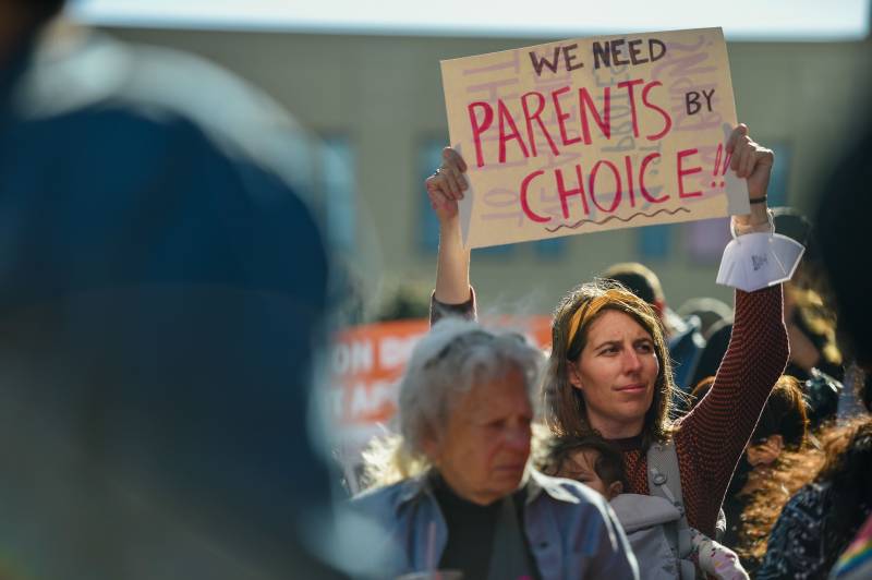 A woman holds a sign that reads "We need parents by choice" in a crowd of people.