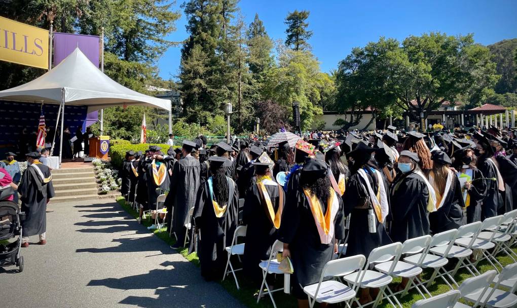 Several people stand in black graduation cap and gowns outside