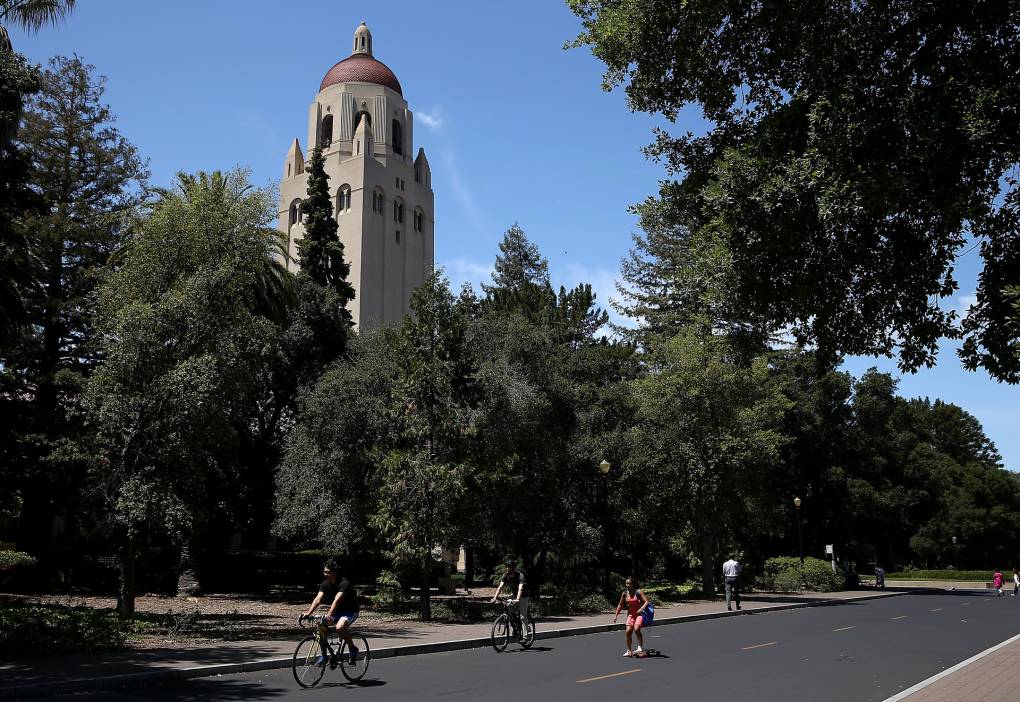 Students ride bikes on a tree-lined street on the campus of Stanford University.