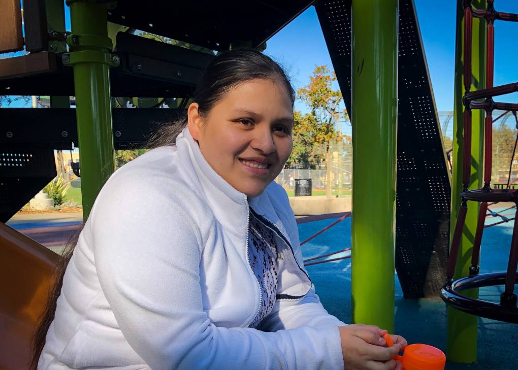 Una mujer con un abrigo blanco está sentada en un parque para niños.