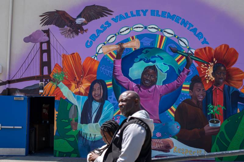 A man and child walk past a multicolored mural of students, a bridge and an eagle.