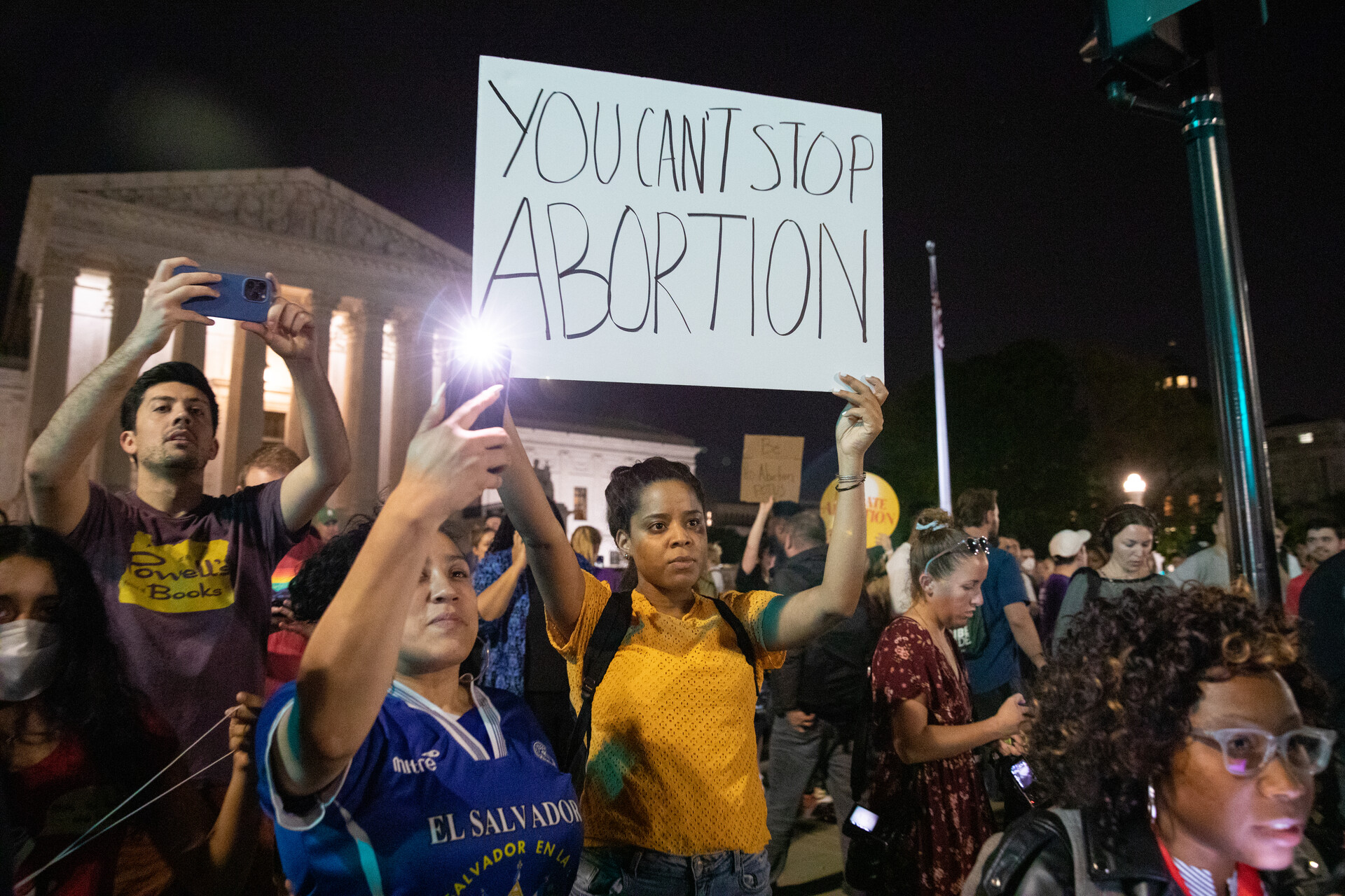 A woman holds large sign saying 'you can't stop abortion' along with other protesters with supreme court building in background