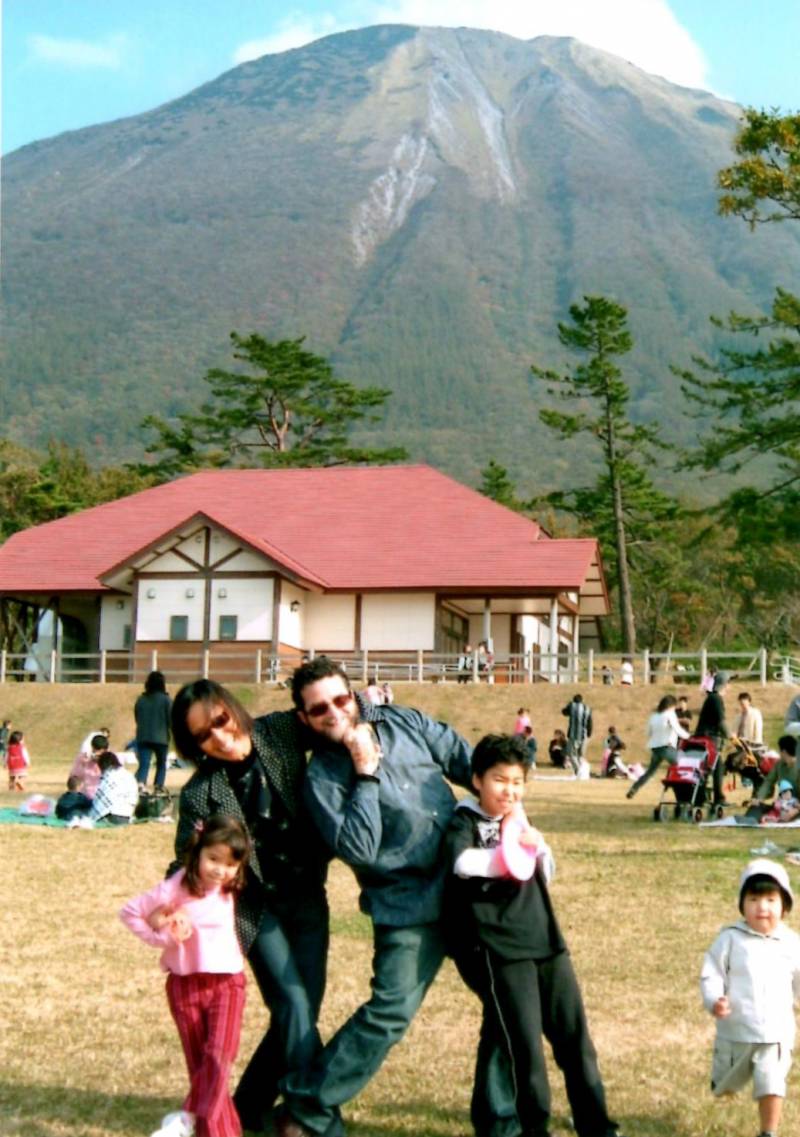 A family — young girl, mom, dad and young boy — pose in a field, with a large mountain in the background.