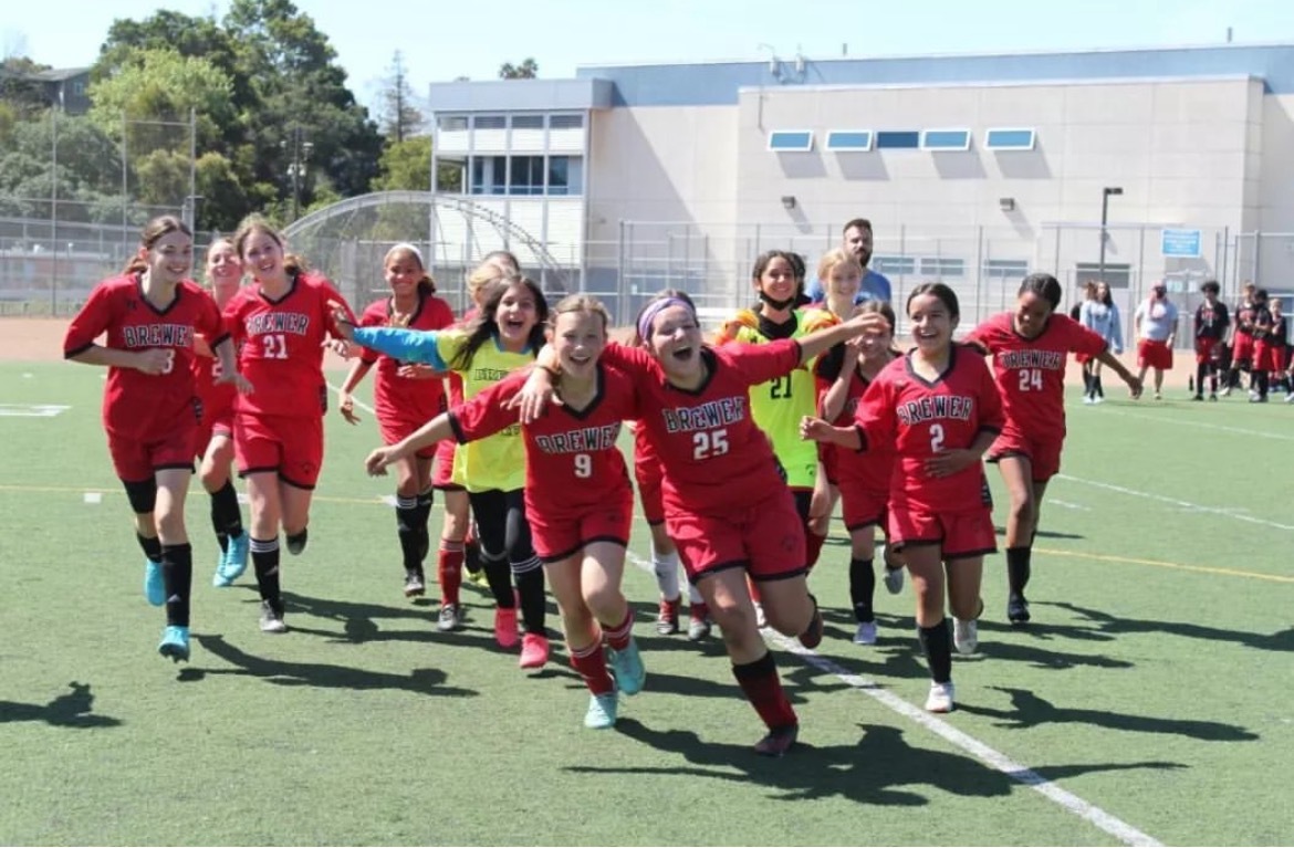 A girls' soccer team celebrates on the field.
