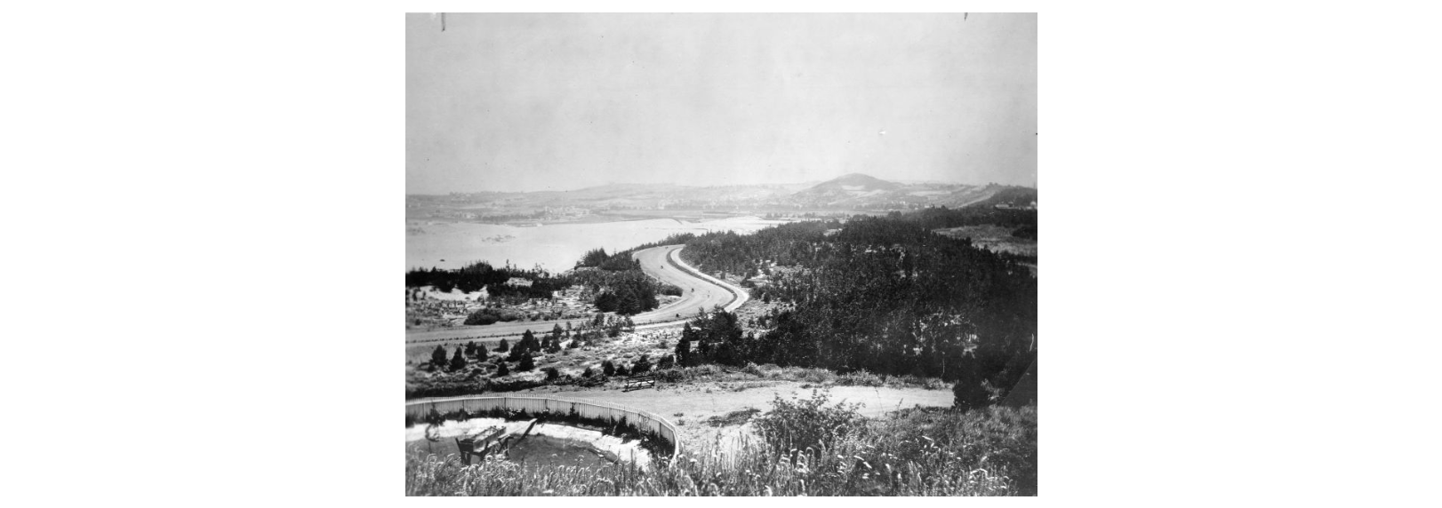 Black and white photo shows rolling sandy hills with grasses and low shrubs. A road winds off into the distance.