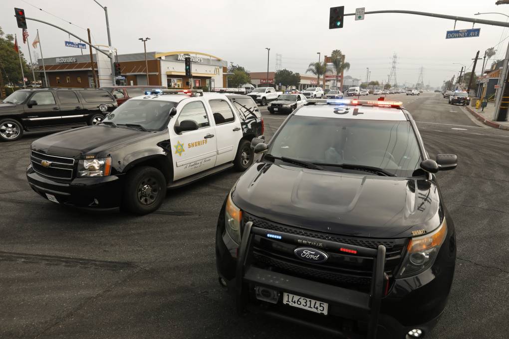 Two black-and-white police SUV's block an intersection. The pavement underneath is marked with large black circles, indicating a car doing donuts in the intersection.