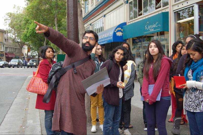 A tour guide points to something, as his tour group stands on the street.