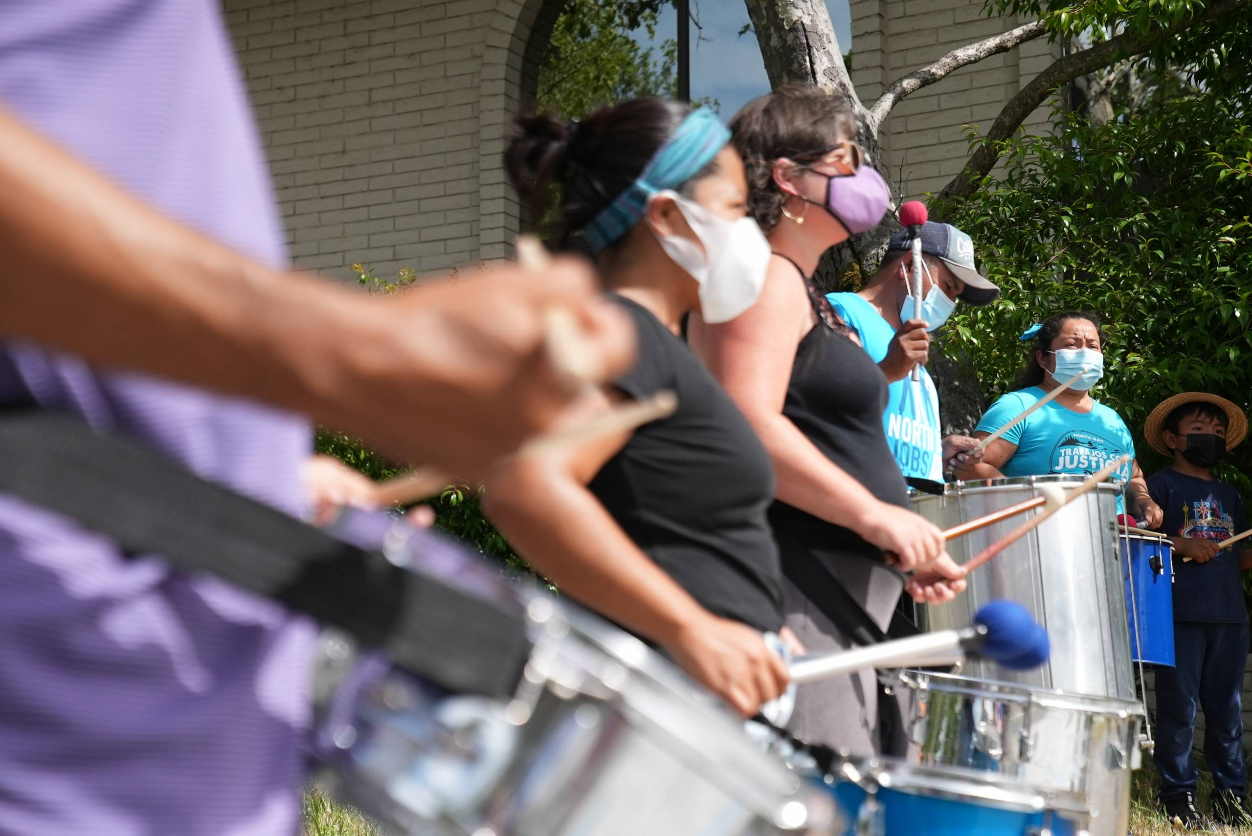 A group of people play the drums outside of an office building.