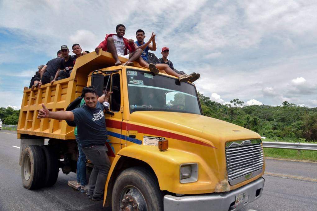 A yellow truck carrying several people drives on the road.