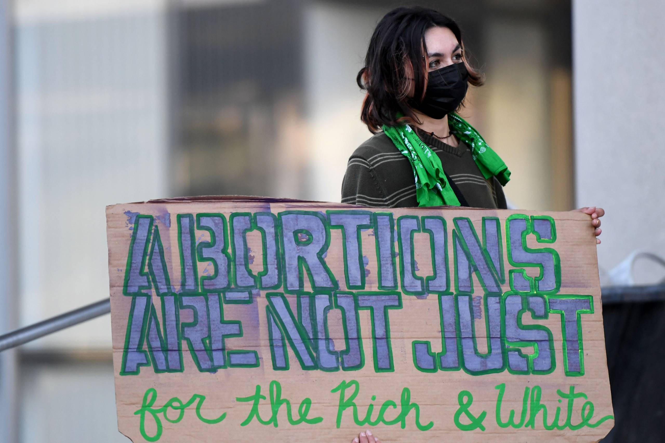 A person bears a very large sign made out of cardboard, which reads: "Abortions are not just for the rich and white."