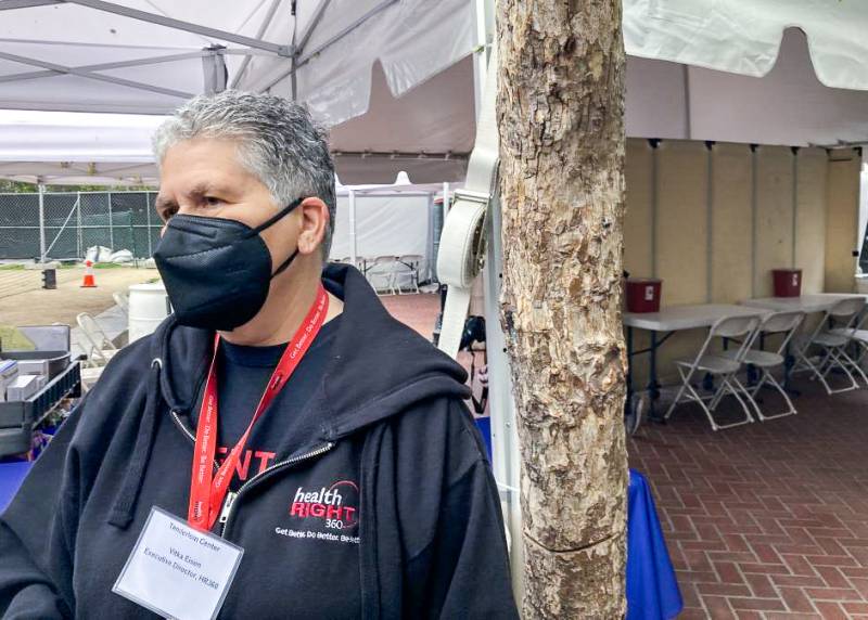 Person wearing mask and lanyard with outdoor tent and plastic chairs in background
