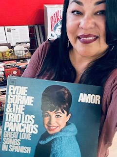 A woman holds a record cover of an album called 'Amor' by Eydie Gormé and The Trio Los Panchos.