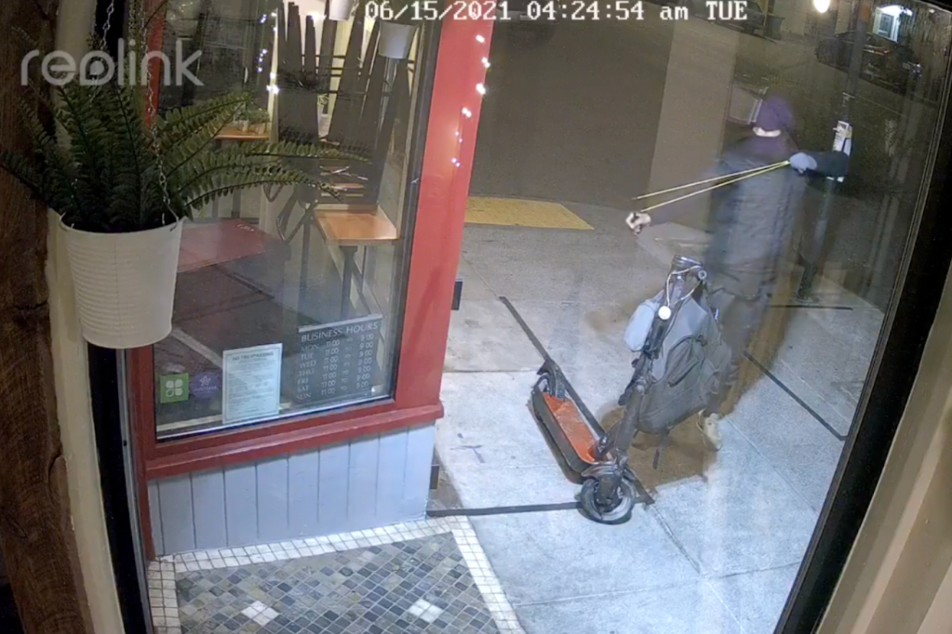Surveillance footage from outside a storefront shows a man pulling back a slingshot.
