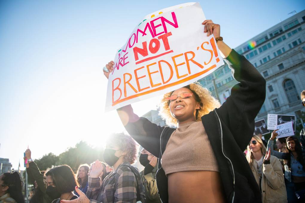 A woman stands in a crowd holding a sign above her head that reads "Women are not breeders!"