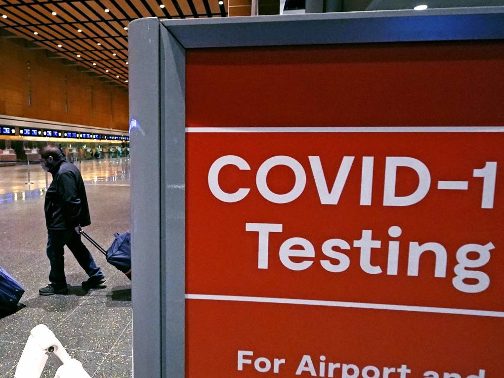 In this photo, travelers pass a sign for COVID-19 testing at Logan Airport in Boston. The Biden administration is lifting its requirement for COVID testing before flying to the U.S.