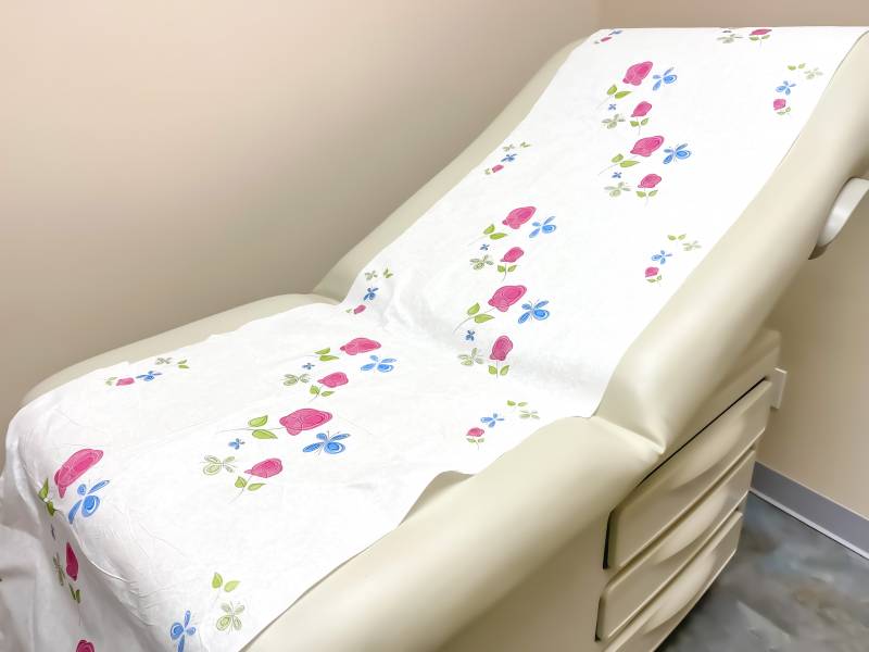 A typical patient chair in cream with a paper covering of pink roses and blue butterflies.