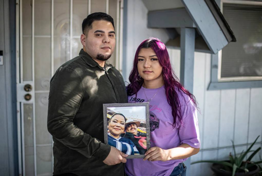 two young adults pose for a portrait while holding a photo of their parents, both of whom died from COVID