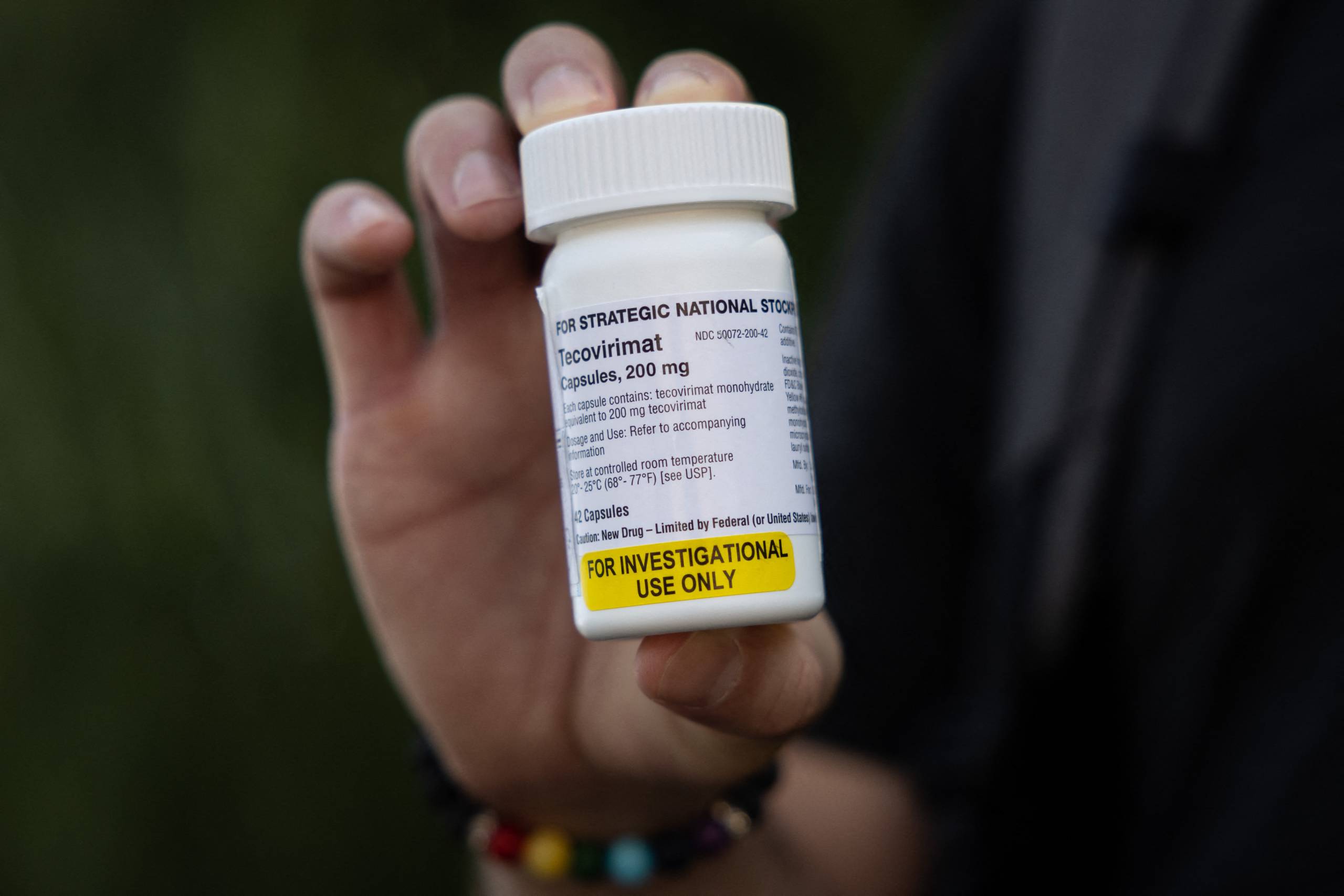 A person's hand holds up a prescription pill cartridge labeled "Tecovirimat."