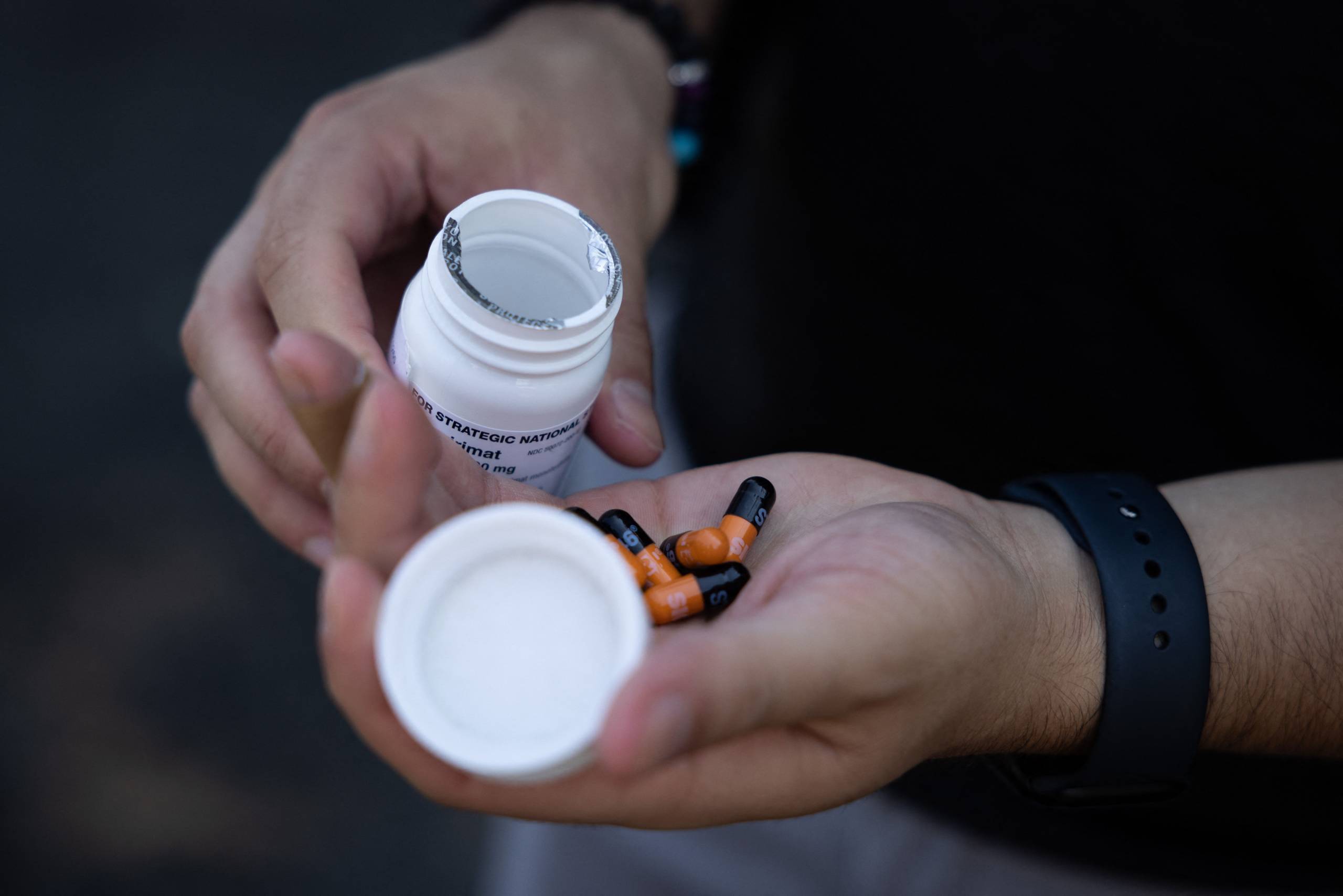 A person empties pills from a prescription pill canister into their other hand.