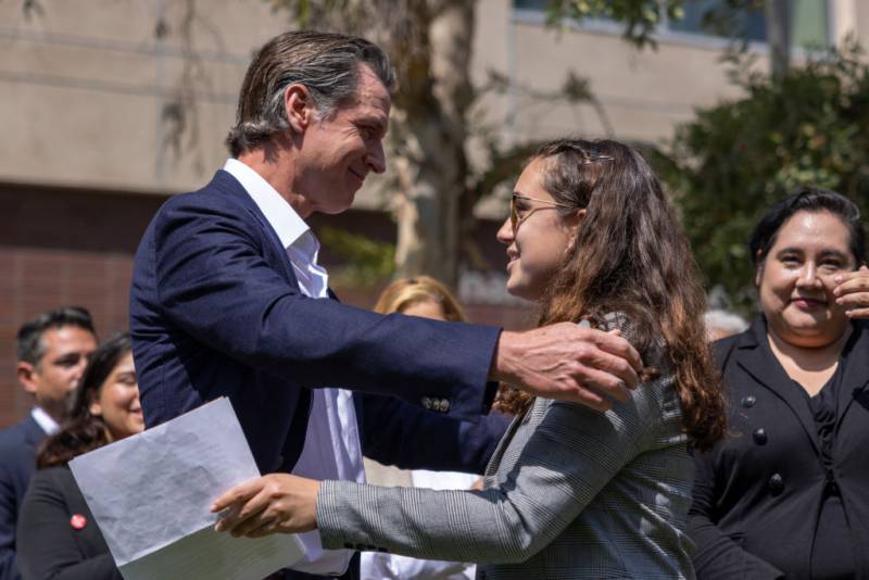Gov. Gavin Newsom embraces a young woman at a press event.