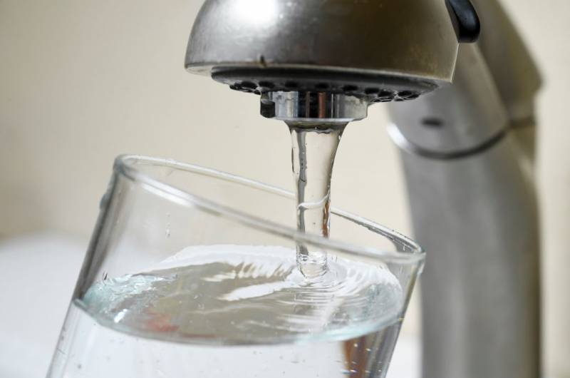 A kitchen sink tap fills a glass of water.