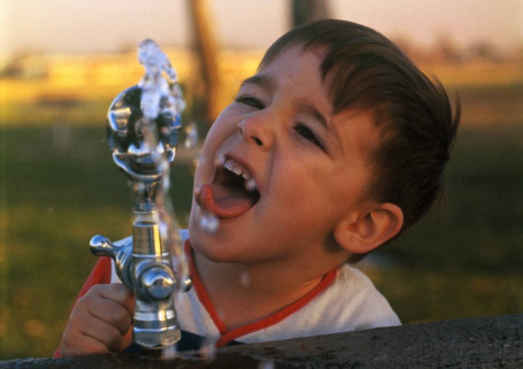a young boy drinks from a water fountain
