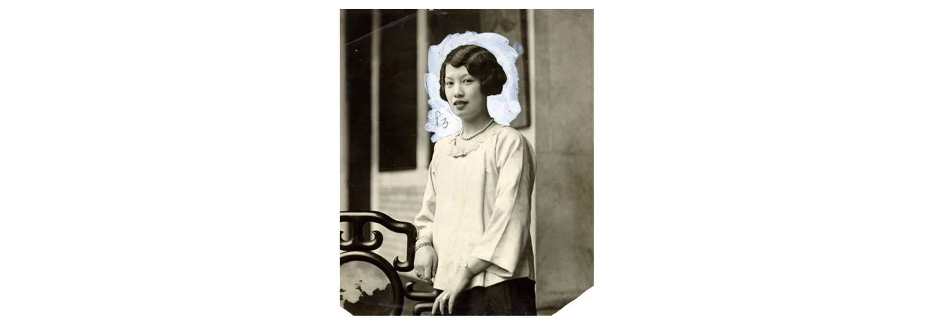 Black and white posed photo of a neatly put together 1920s Asian woman. She has a wave in her hair and is wearing a long sleeved white shirt.