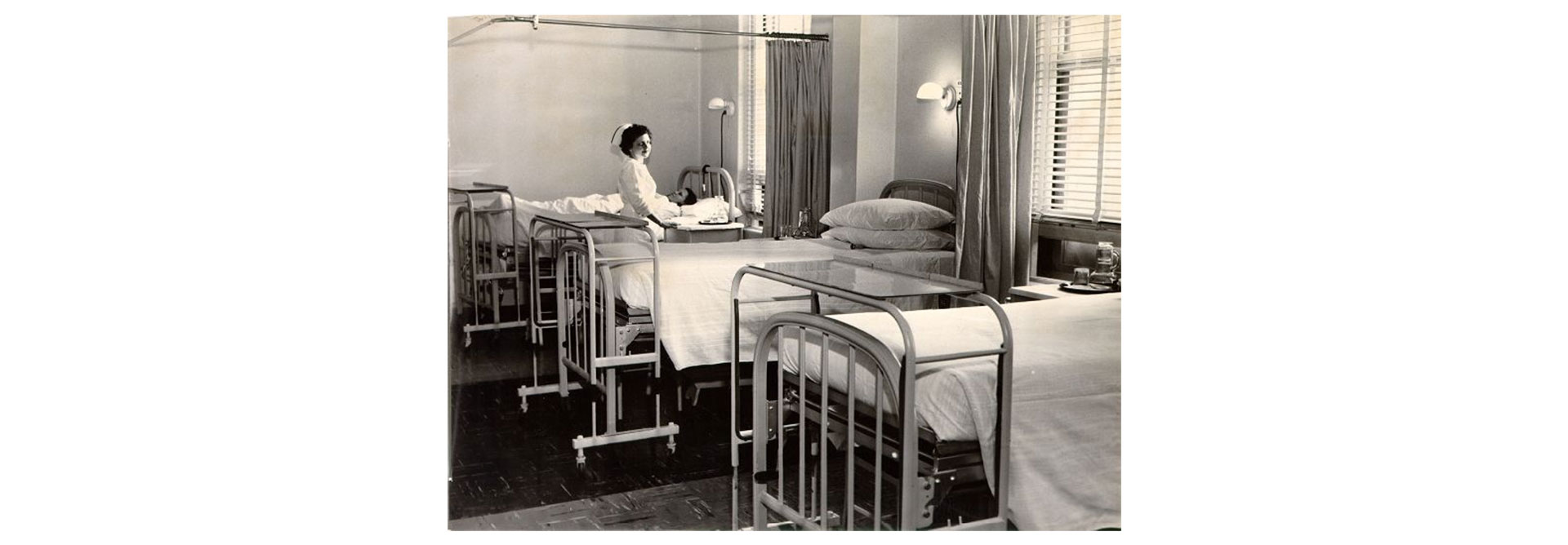 In the foreground, three empty hospital beds are lined up against a wall.  Near the last bed is a nurse in an old-fashioned uniform