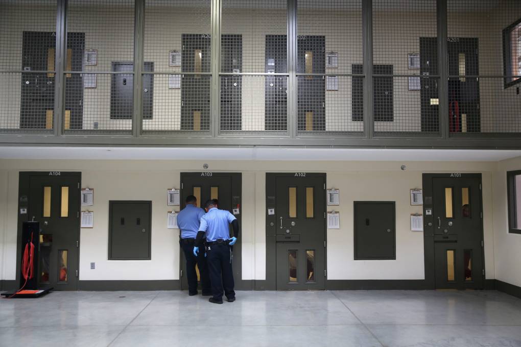 A wide shot of two men wearing blue standing in front of a green door at a detention facility.
