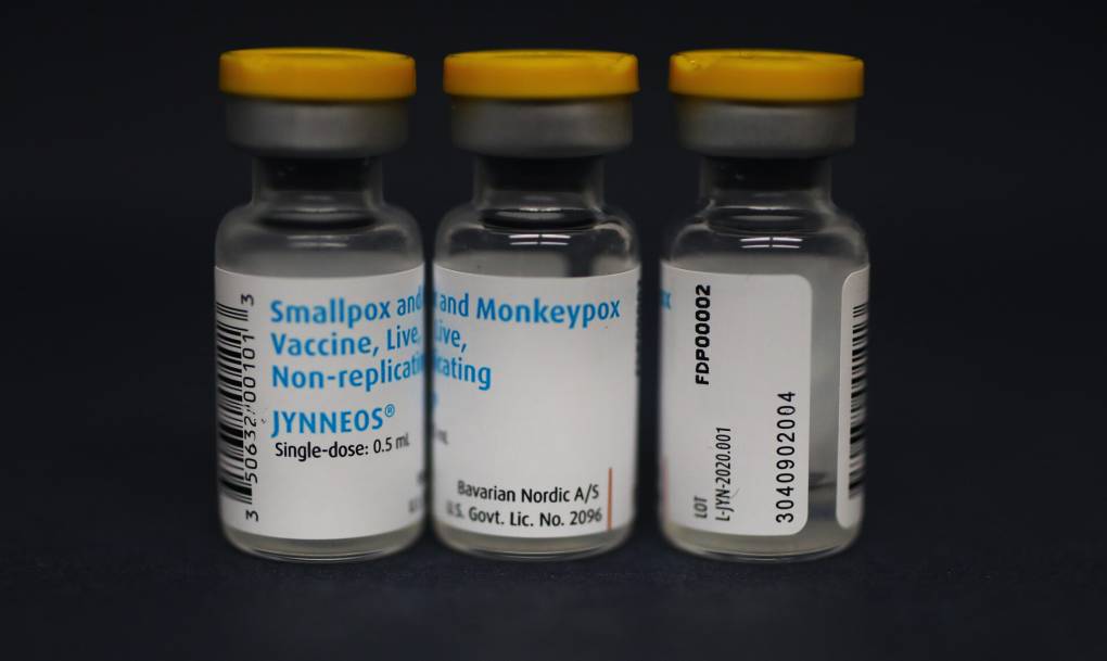 Three vials of the monkeypox vaccine Jynneos photographed side by side, standing up, against a dark background.