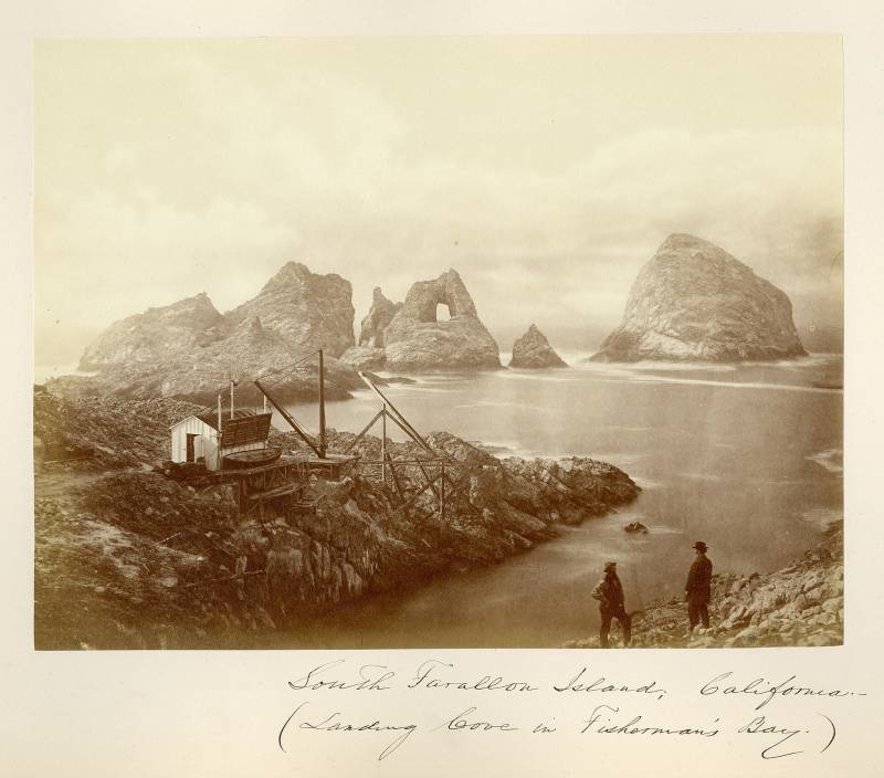 A black and white photo taken on the Farallon Islands. A boat has been pulled onto the top of the rocks by a wooden, crane-like device. 