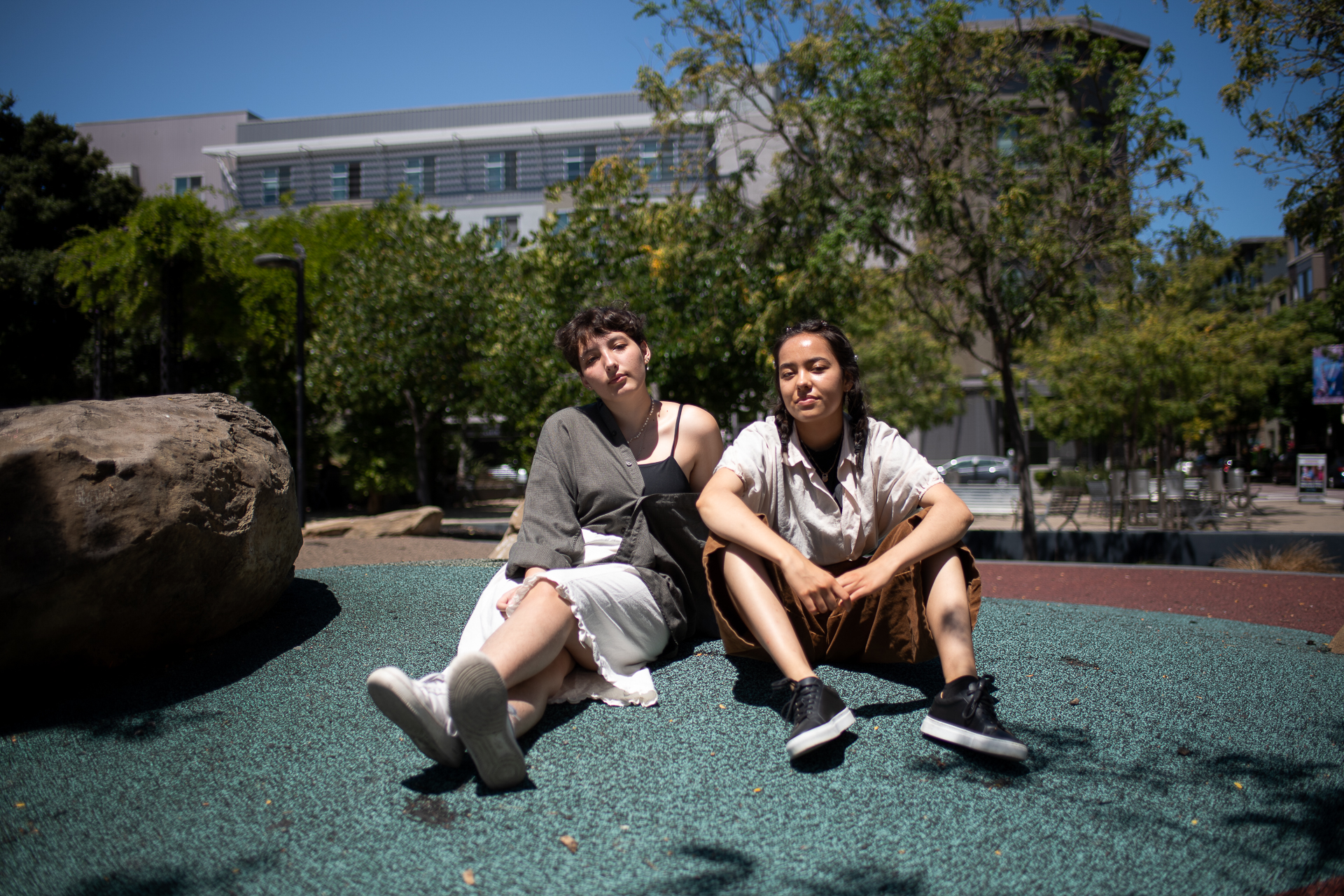 Two girls sit on the ground in front of a large building.