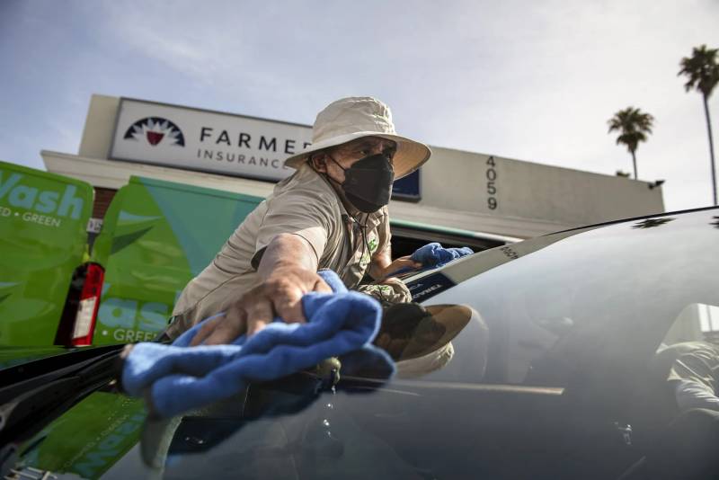 a man in a black mask wipes a windshield at a car wash
