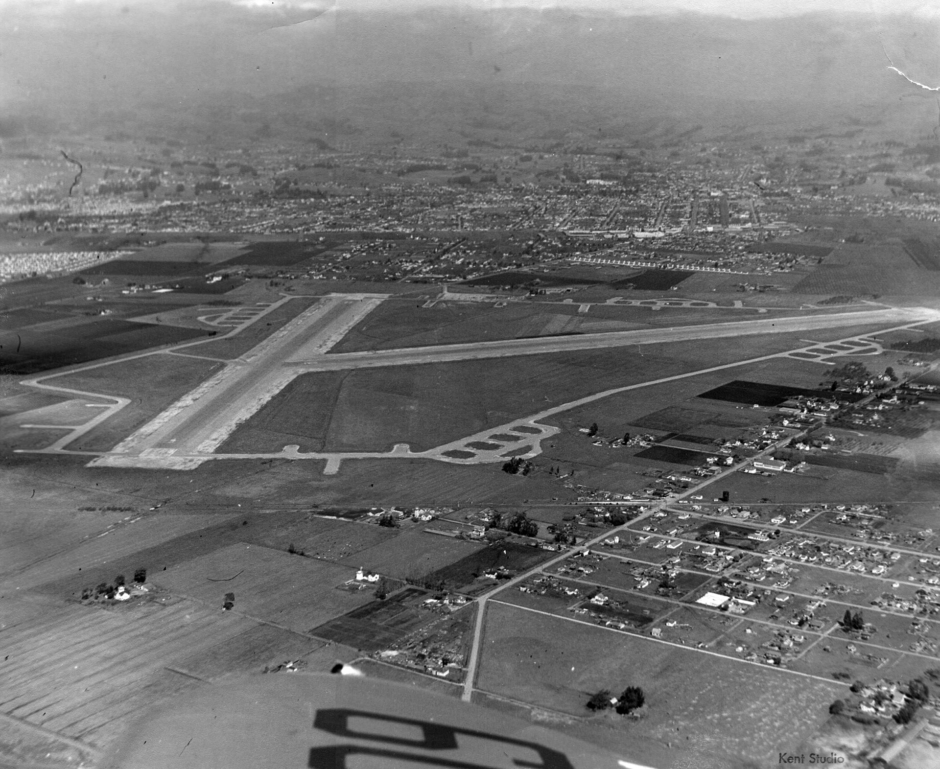 Black and white photo from above showing an airport runway next to a small town of about twelve blocks.