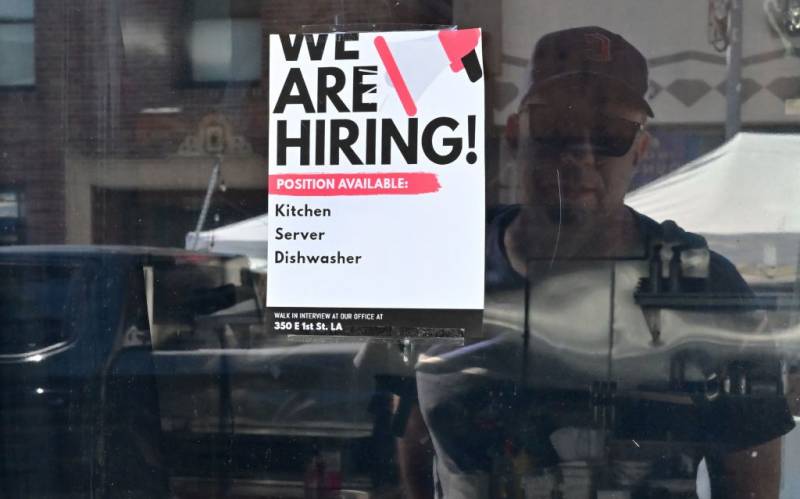 A window sign that says 'We Are Hiring' with the reflection of a man looking at it.