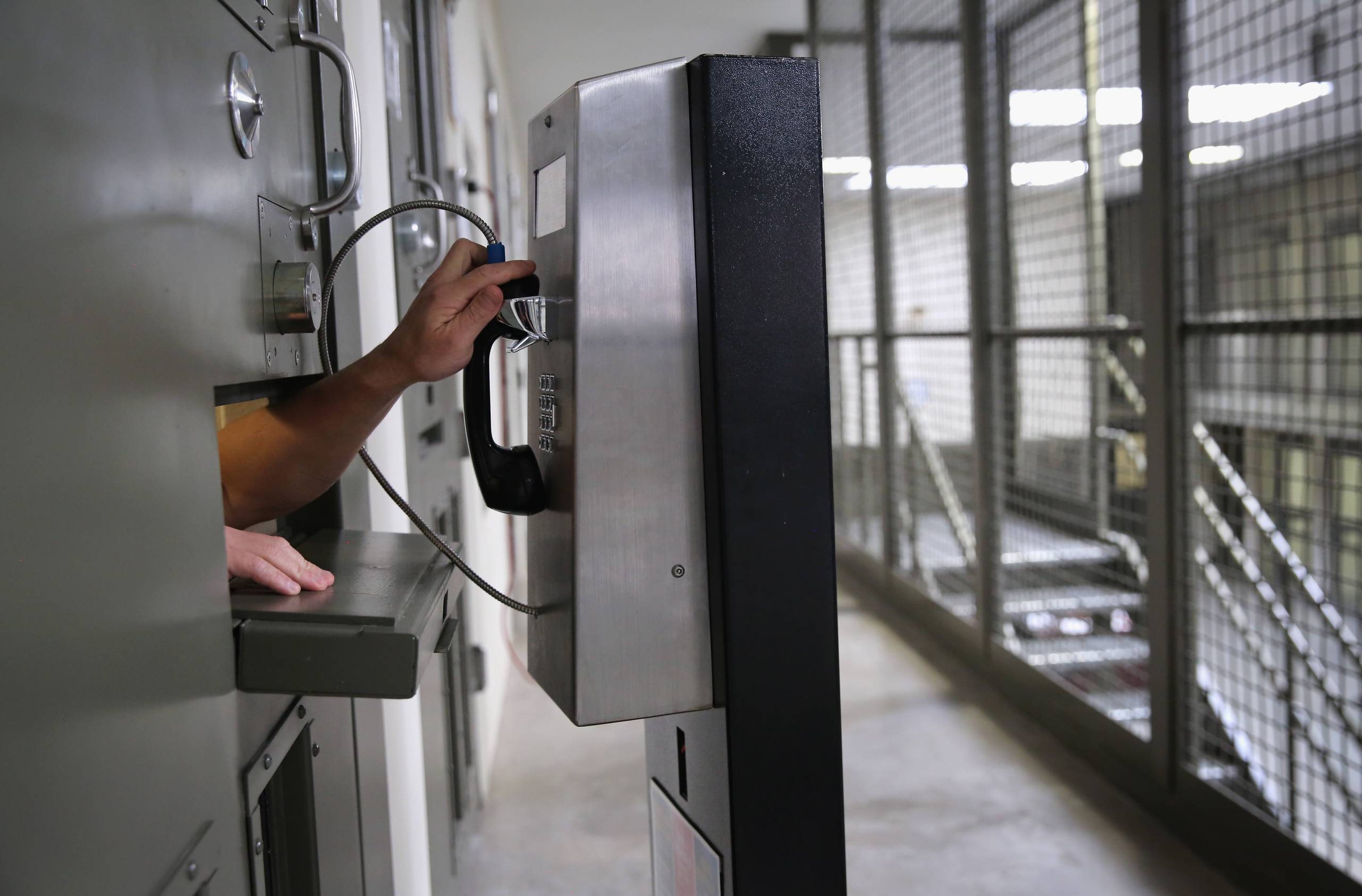 reaching out of a cell to use a payphone in a detention center