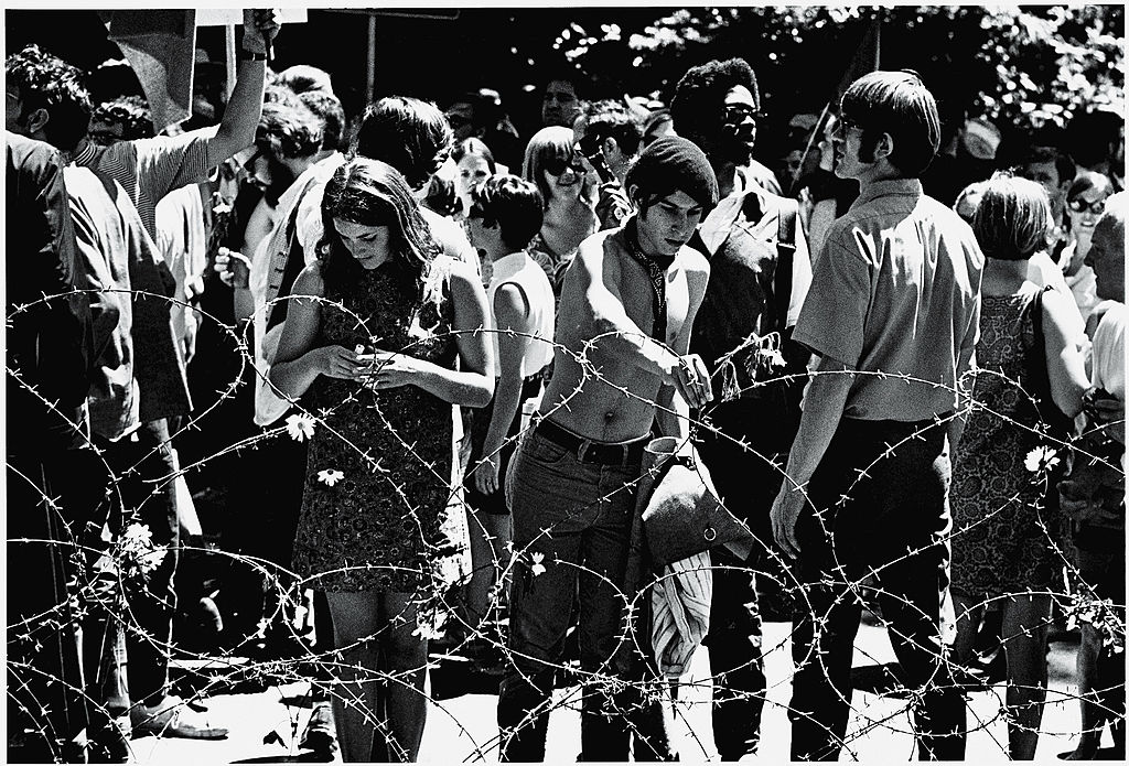 A black and white photo of several people standing outside behind barbed wire.